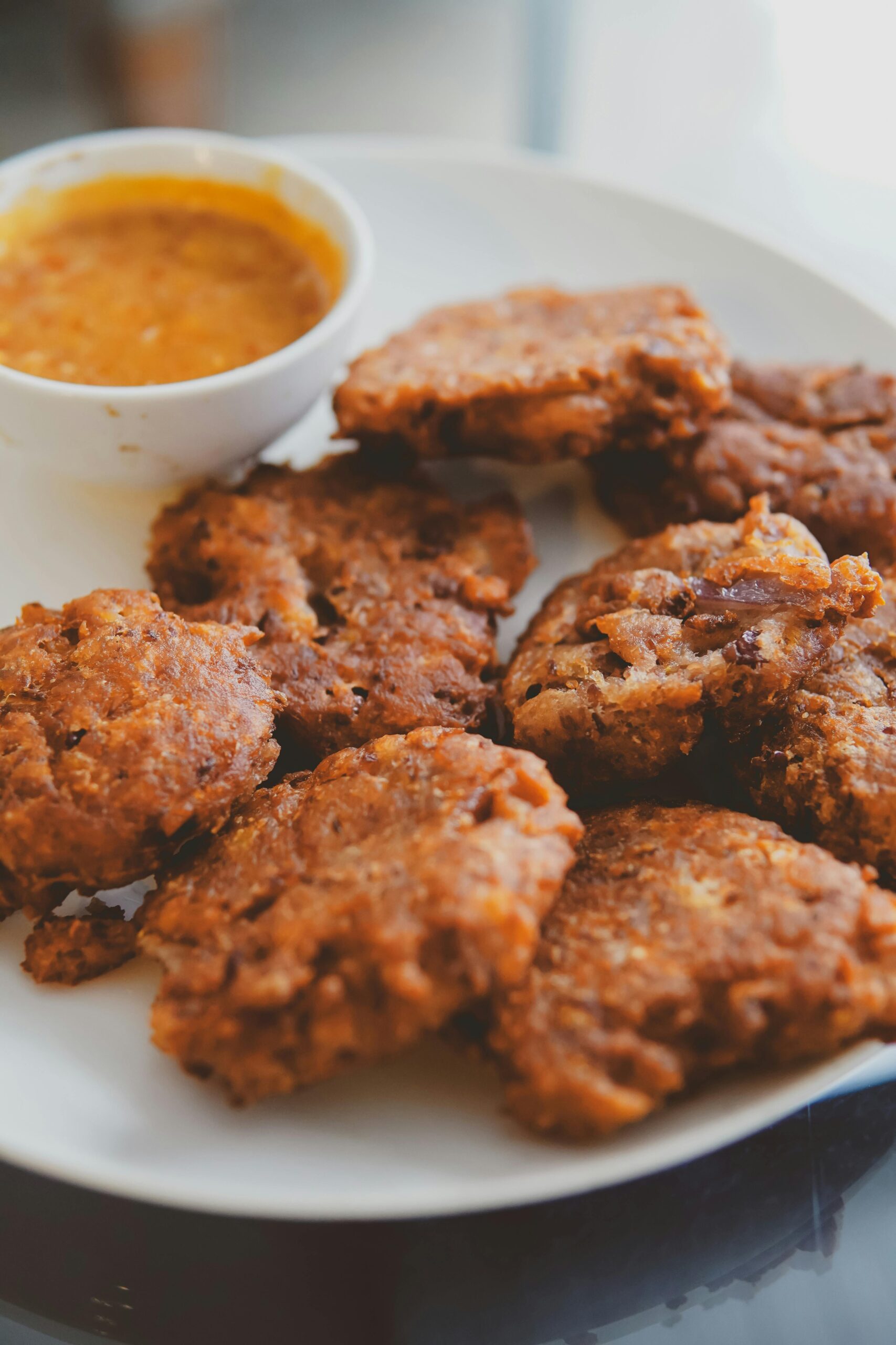 Crispy homemade fritters served with a savory dipping sauce on a white plate.